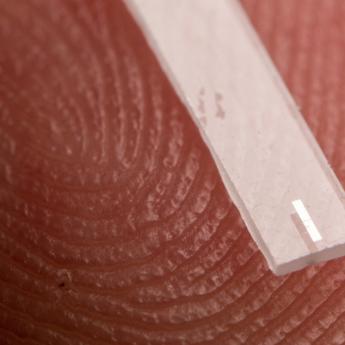 A qubit (the small rectangle) is set onto a sapphire substrate, which sits upon a fingertip to show scale.